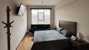 Une chambre à coucher comprenant un lit, une table de chevet, une lampe et un téléviseur fixé au mur.
