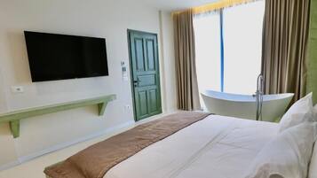 Een hotelkamer met een bed, een aan de muur bevestigde televisie, een groene deur, een raam met gordijnen en een kleine tafel.