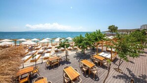 Une terrasse au bord de la plage, dotée de chaises longues et de tables, avec vue sur la mer.