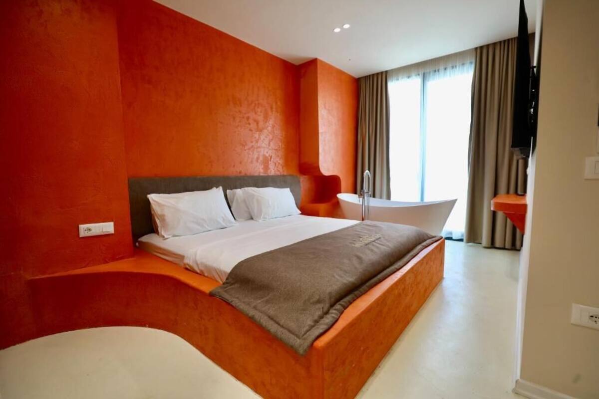 Moderni hotellihuone, jossa on suuri sänky, kylpyamme ja suuri ikkuna, jossa on verhot.