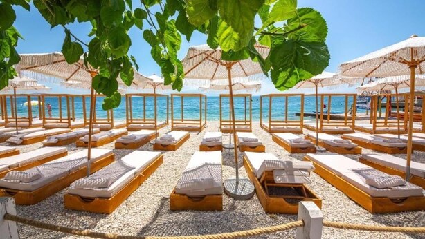 Un hôtel situé en bord de mer, avec des rangées de chaises longues et de parasols, une vue dégagée sur la mer et une clôture en bois.
