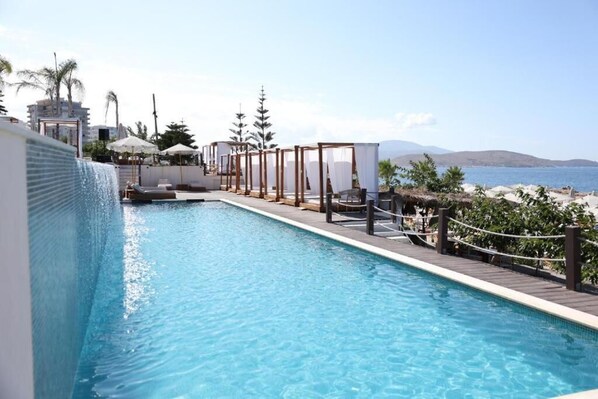 A swimming pool with a view of the sea, surrounded by lounge chairs and umbrellas. - San Angelo Luxury Studios - Adults Only 100m from main resort (Sarande)
