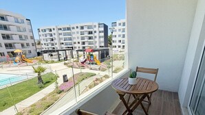 Un balcón con una mesa y sillas de madera, vista a un parque infantil y edificios residenciales al fondo.