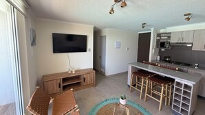 Una cocina moderna con televisor de pantalla plana, taburetes de madera en una barra y una isla central.
