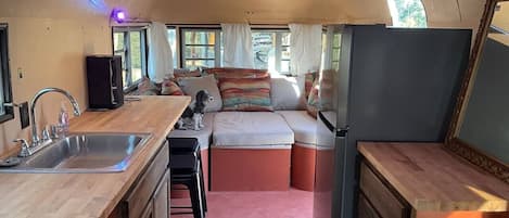 Un espacio interior compacto con kitchenette, zona de estar y un perro.