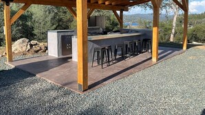 Un espace cuisine extérieur doté d’un bar avec des tabourets, d’un barbecue intégré et offrant une vue sur le paysage environnant.
