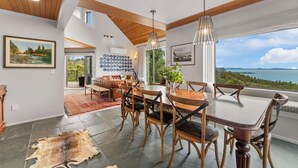 Un comedor con una mesa y sillas de madera, una lámpara colgante y vista al mar.