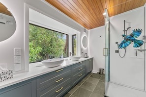 A modern bathroom with a large window, two sinks, a shower, and a bird mural.