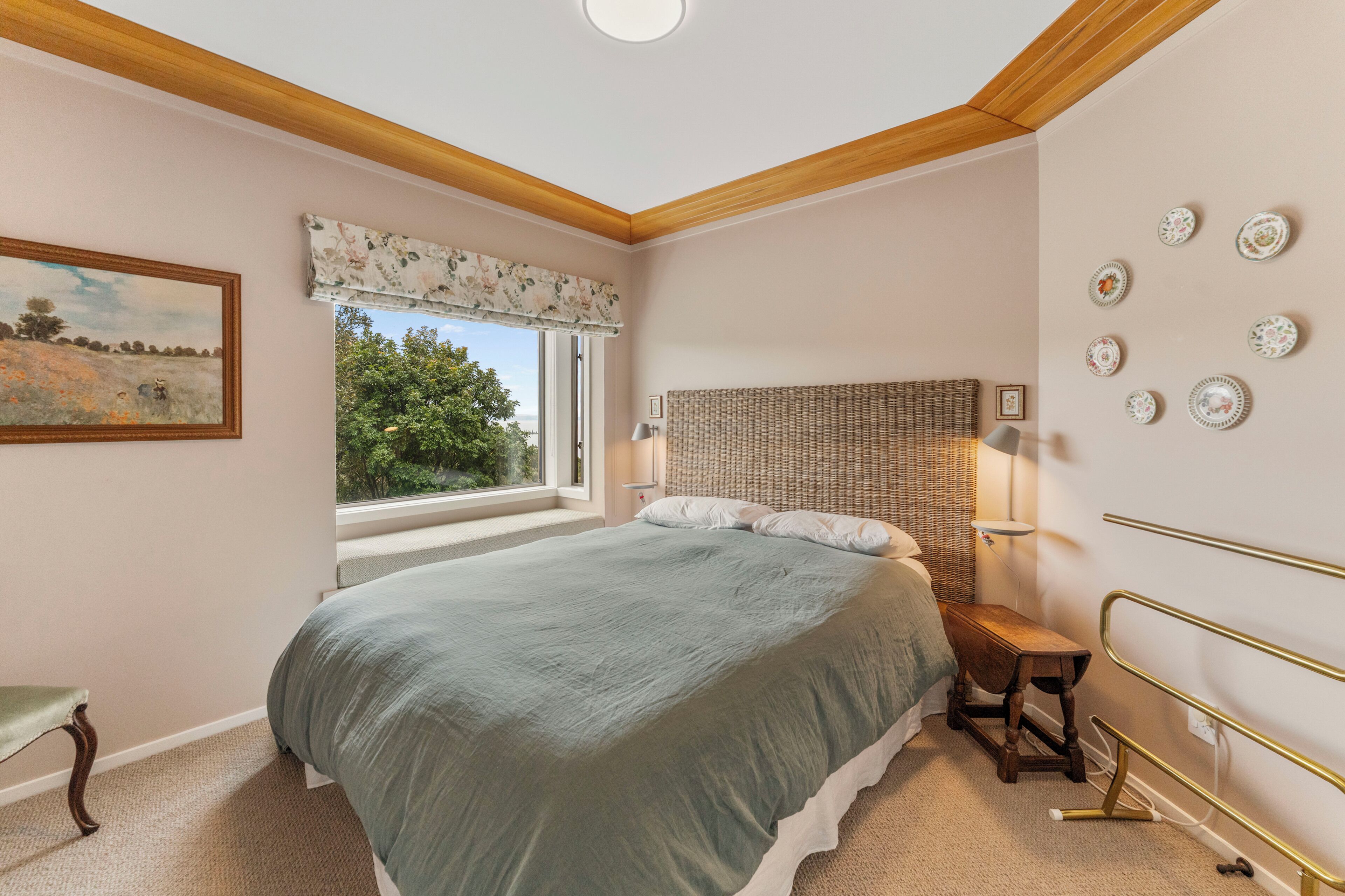 A bedroom with a bed, a window with a view, a bedside table, and a wall with decorative plates.