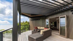 Una terraza moderna al aire libre con un sofá y reposapiés, una puerta corrediza de vidrio que da a un espacio interior, y vista al océano.