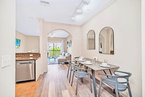 A modern kitchen with a dishwasher, a dining area with a table and chairs, and a view of the outside. - Upstay Disney Pet Friendly Condo w Pool Spa Games (Winter Garden)