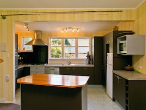 A kitchen with a central island, a stove, a sink, cabinets, and a window with a view.