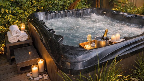 Un jacuzzi con velas, una botella de champán y toallas sobre una terraza de madera.