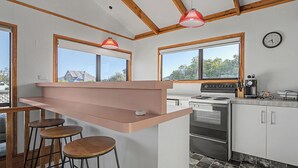 Eine Küche mit einer zentralen Kochinsel, Barhocker, einem Herd, einer Kaffeemaschine und einer Uhr an der Wand.