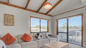 Ein geräumiges Wohnzimmer mit einem beigen Sofa, einem Couchtisch und großen Fenstern mit Blick ins Freie.