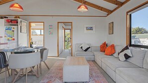 Ein geräumiger Wohnbereich mit einer Couch, Hocker, Esstisch, Stühlen und einer Küchenzeile mit Kühlschrank.
