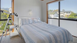 Ein Schlafzimmer mit einem Bett, einem Teleskop und Blick auf Häuser durch große Fenster.