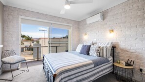 A bedroom with a bed, a chair, a table, and a balcony with a view. - Walk, Relax, Enjoy - stylish townhouse, steps from beaches and shops (South West Rocks)