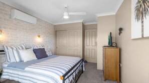 Ein Schlafzimmer mit einem Bett, einem Deckenventilator, einer Wand-Klimaanlage, einem Holzschrank und einer Tür.