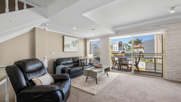 A spacious living area with a leather sofa, a coffee table, and a view of the outside through large sliding glass doors. - Walk, Relax, Enjoy - stylish townhouse, steps from beaches and shops (South West Rocks)