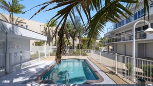 A swimming pool surrounded by white fences, palm trees, and a building with balconies. - Walk, Relax, Enjoy - stylish townhouse, steps from beaches and shops (South West Rocks)
