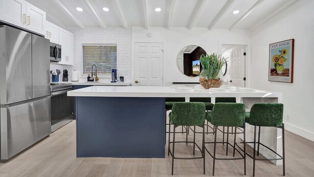 Una cocina moderna con una isla central, taburetes de bar, electrodomésticos de acero inoxidable y un espejo grande.