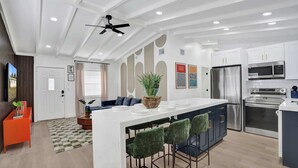 Una cocina moderna con una isla central, taburetes de bar, electrodomésticos de acero inoxidable y un ventilador de techo.