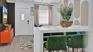 Un comedor moderno con una mesa blanca, sillas verdes y un centro de mesa decorativo con una planta.