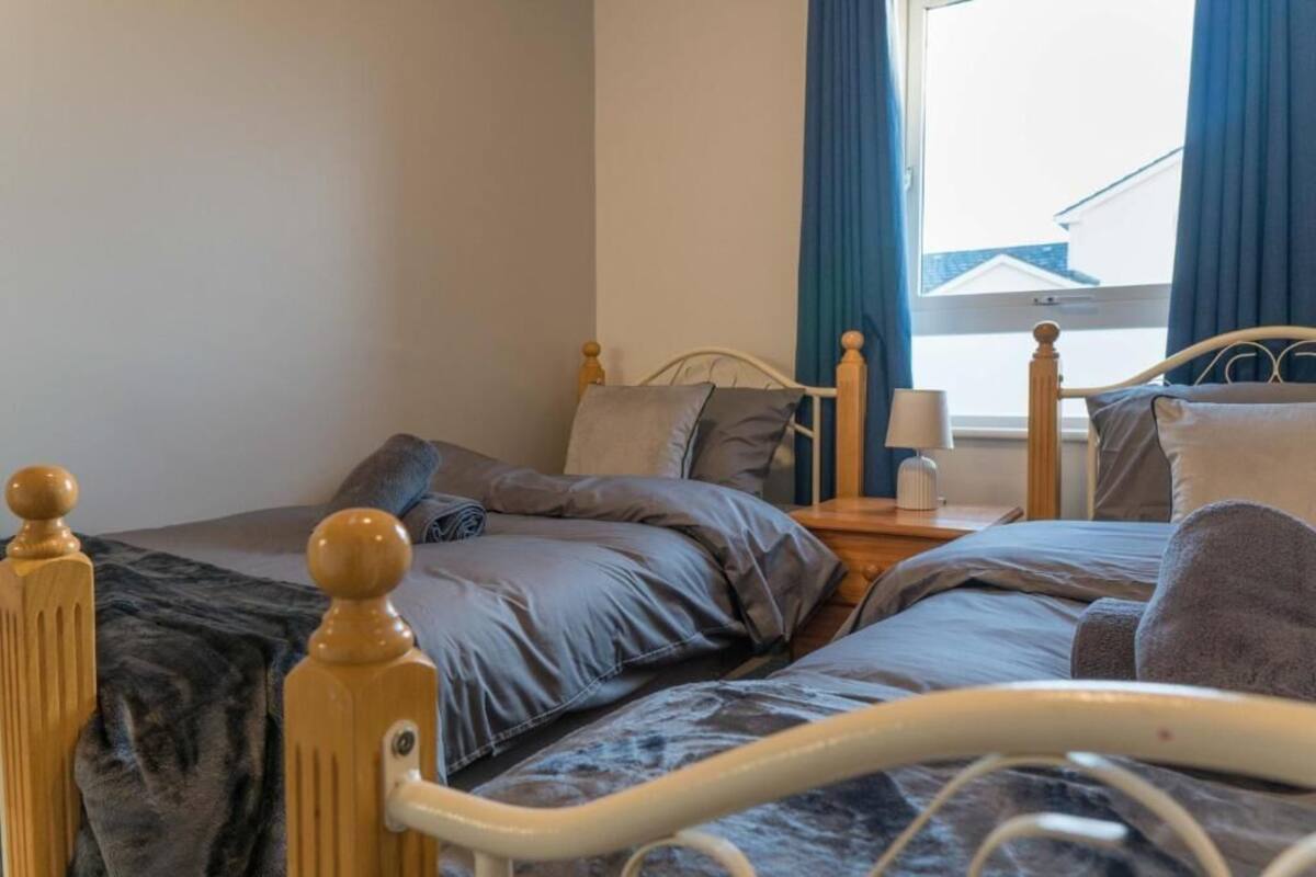 A bedroom with two beds, wooden headboards, a bedside table with a lamp, and a window with curtains.