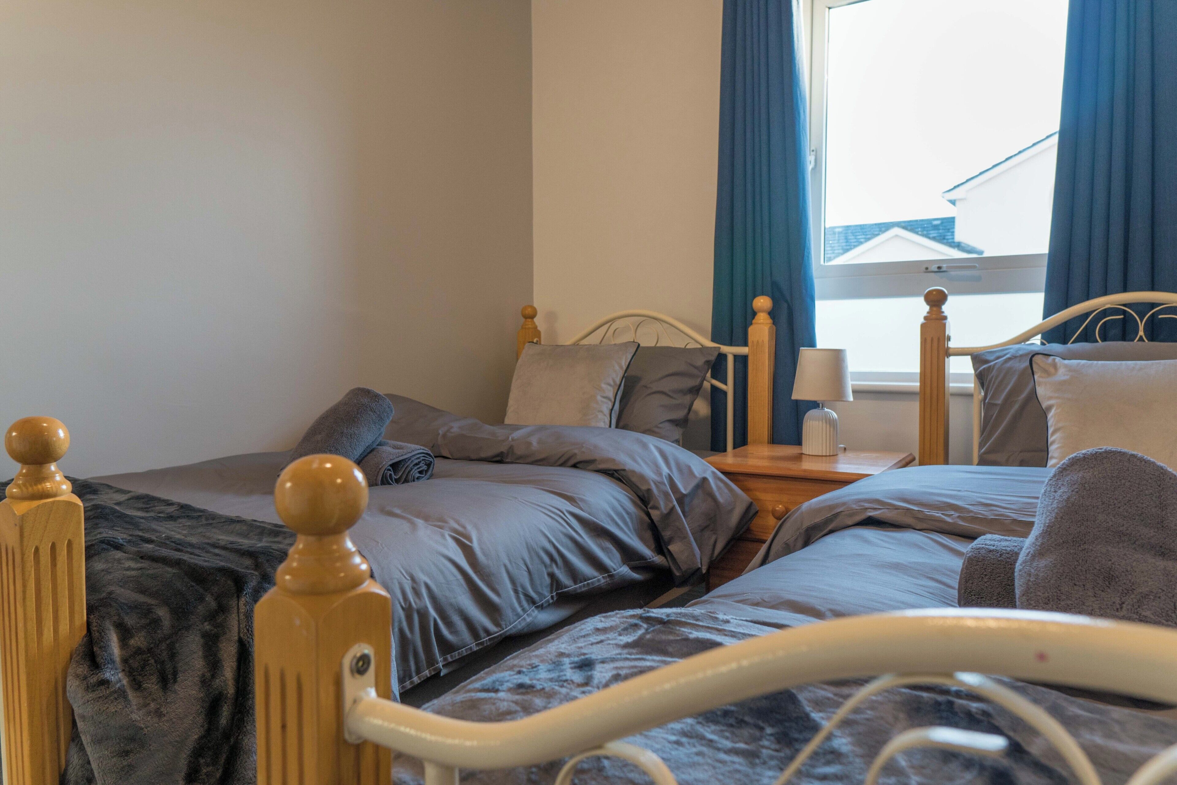 Een slaapkamer met twee bedden, een nachtkastje, een lamp en een raam met gordijnen.