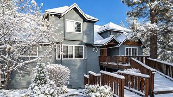 A two-story house with a covered deck and a snow-covered landscape.