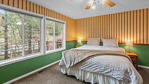 Une chambre dotée d’une grande fenêtre, d’un ventilateur de plafond et d’un lit avec deux tables de chevet.