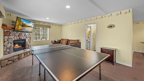 Un salon avec une table de ping-pong, une cheminée en pierre et un canapé.