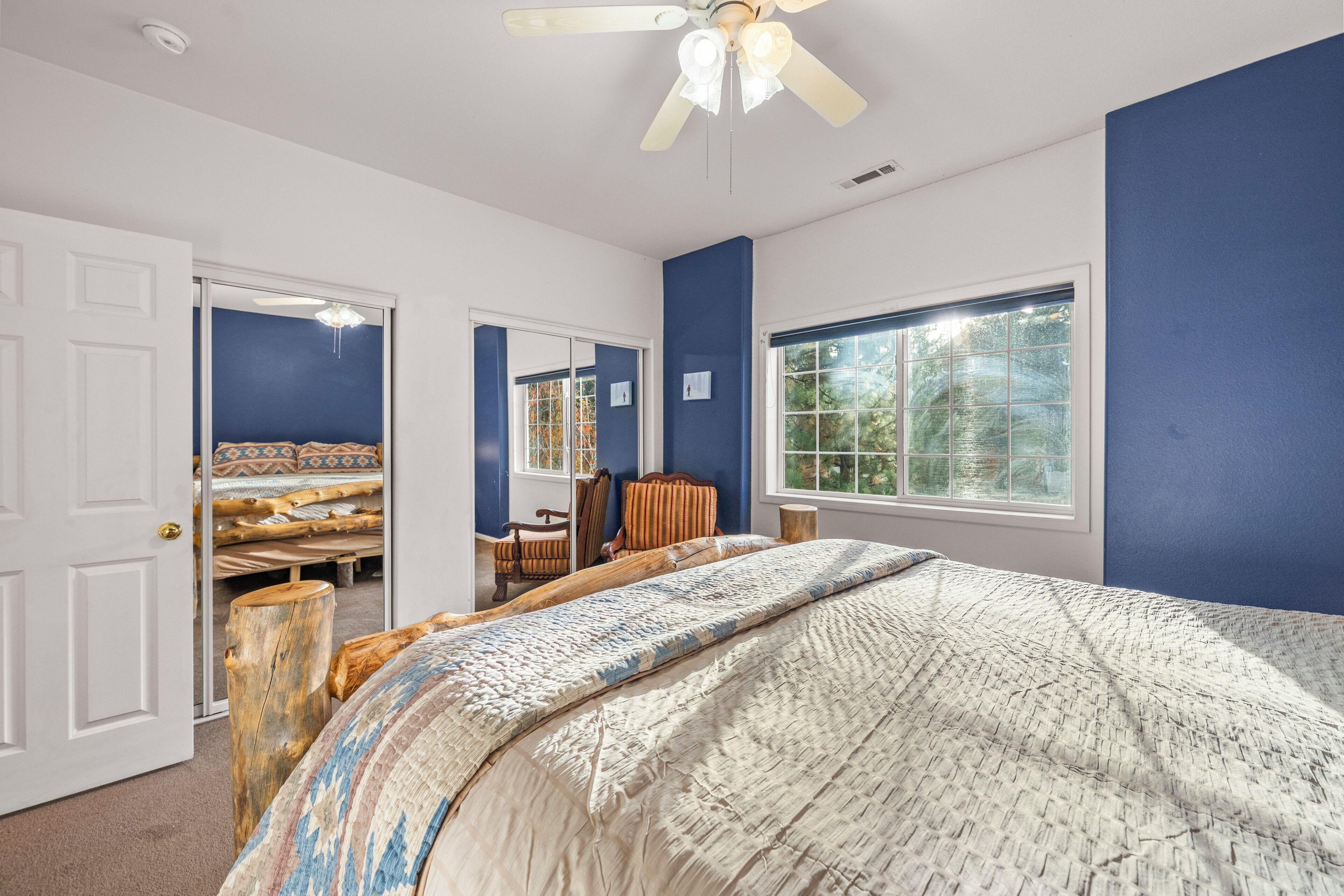 A bedroom with a large bed, a ceiling fan, and a window with a view of trees.