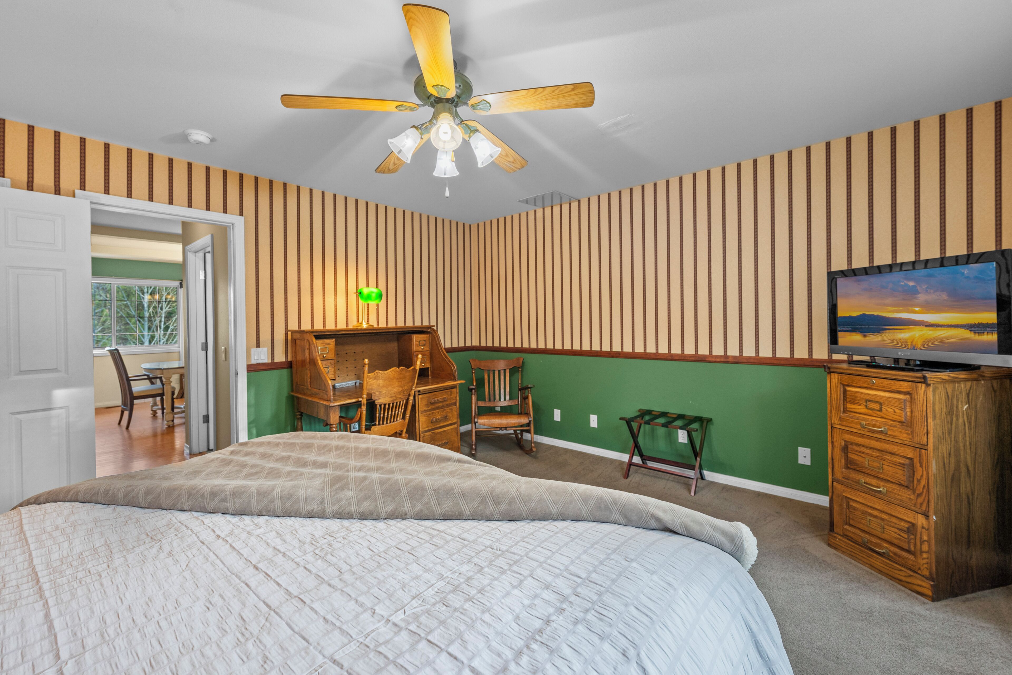 Un dormitorio con una cama grande, ventilador de techo, televisor y cómoda.
