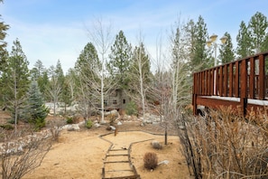 Une terrasse en bois avec une rambarde en métal, entourée d’arbres et sous un ciel dégagé.