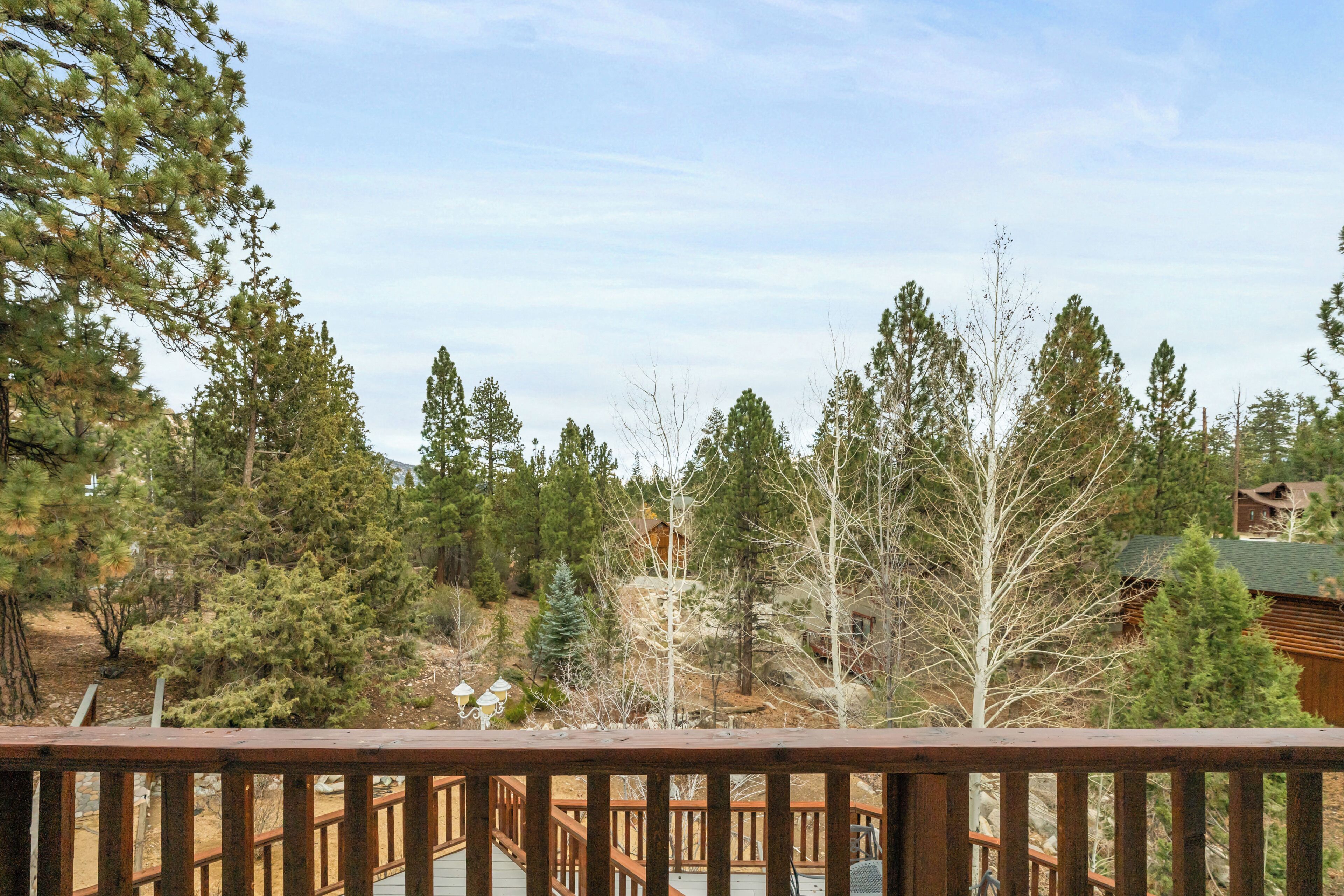 A wooden deck with a view of a mountainous area, surrounded by evergreen trees.