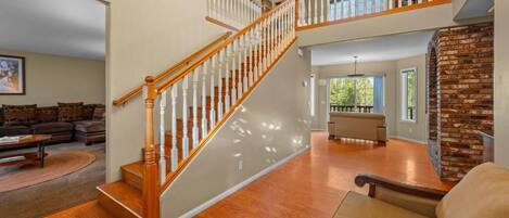 A spacious living area with a wooden staircase, a brick accent wall, and a cozy seating arrangement.