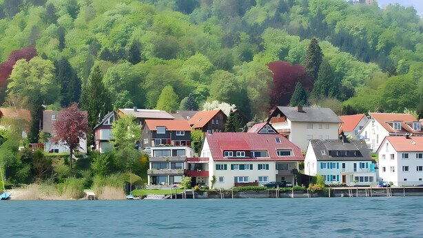 A lakeside residential area with houses, a dock, and a hill with trees. - Guest House 'Kleines Zimmer Am See' with Shared Garden and Wi-Fi (Bodman-Ludwigshafen)