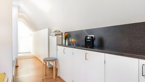 A modern kitchen with white cabinets, a black countertop, a coffee maker, and a vase with flowers. - Guest House 'Kleines Zimmer Am See' with Shared Garden and Wi-Fi (Bodman-Ludwigshafen)