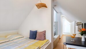 A modern, compact bedroom with a bed, pillows, a hanging light fixture, and a small table with glasses and a vase. - Guest House 'Kleines Zimmer Am See' with Shared Garden and Wi-Fi (Bodman-Ludwigshafen)