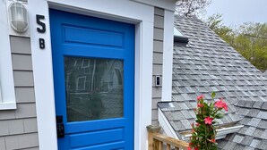 A blue door with a window, a wooden deck, and a potted plant with pink flowers. - Ocean light Deck + Patio • Central P-Town (Provincetown)