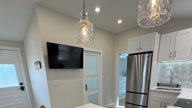 A modern kitchen with a large island, stainless steel appliances, and a unique crystal pendant light. - Ocean light Deck + Patio • Central P-Town (Provincetown)