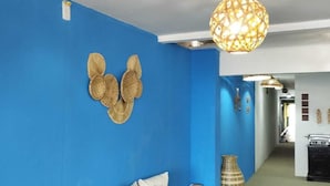 A room with a blue wall, a bench with pillows, a hanging light fixture, and a wicker vase. - Pousada Pé no Mar (Japaratinga)