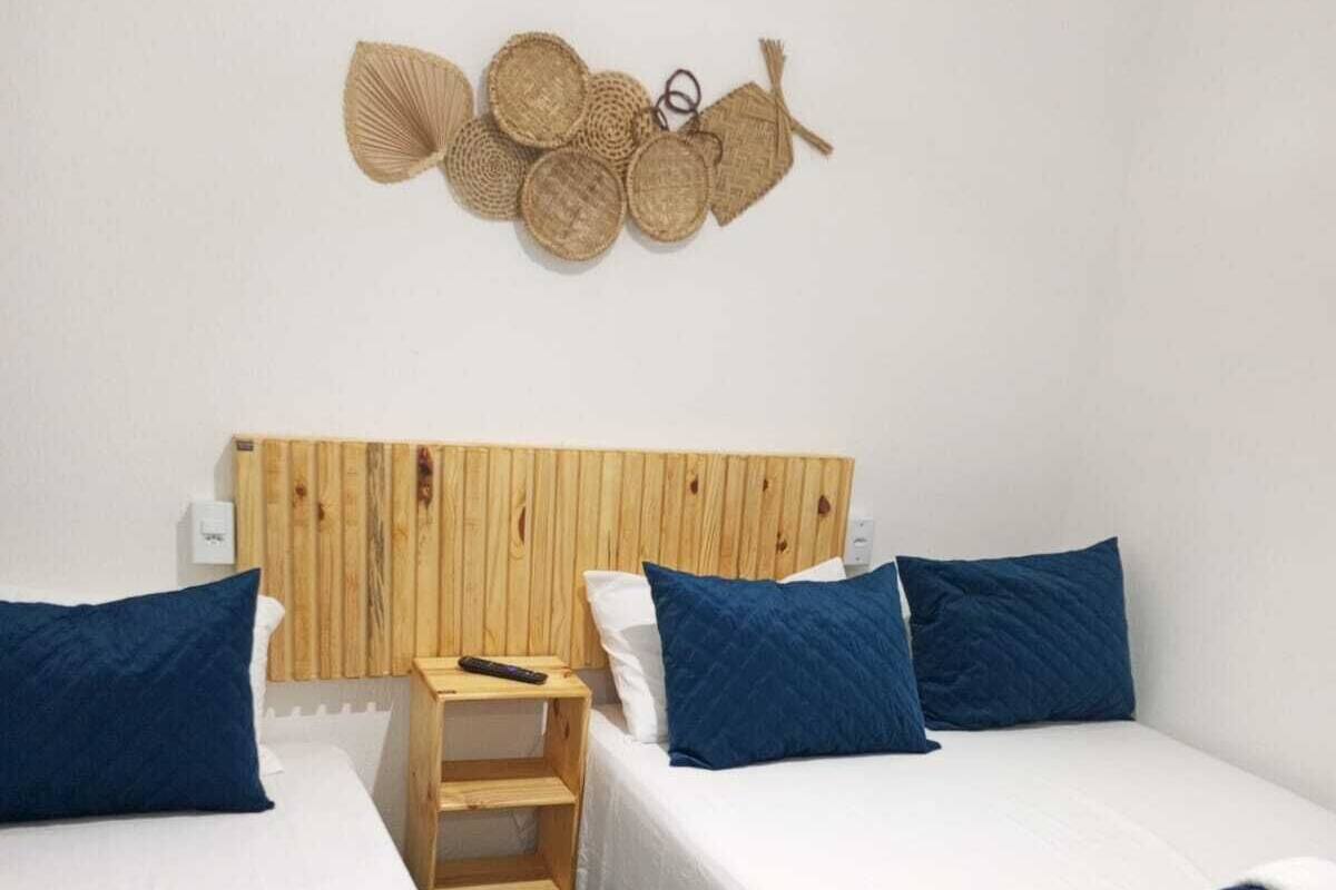 A room with two beds, each with a blue blanket and pillow, a wooden headboard, and a wall-mounted decorative item.