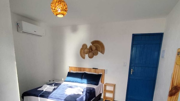 A bedroom with a bed, a blue door, a wall-mounted air conditioner, and a hanging light fixture. - Pousada Pé no Mar (Japaratinga)