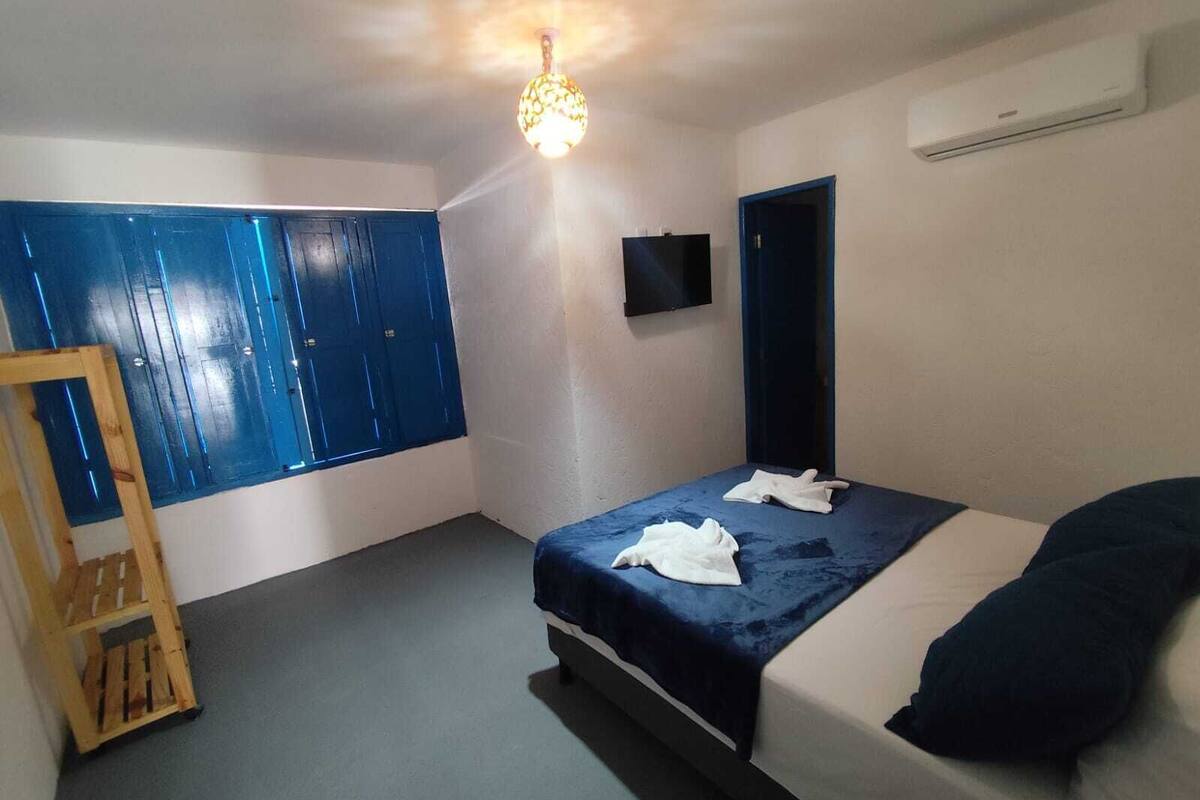 A bedroom with a bed, a wooden ladder, a TV, and a ceiling light.