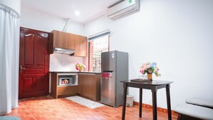 Una cocina compacta con refrigerador, un mueble de madera, una ventana con barrotes y una pequeña mesa con un florero.