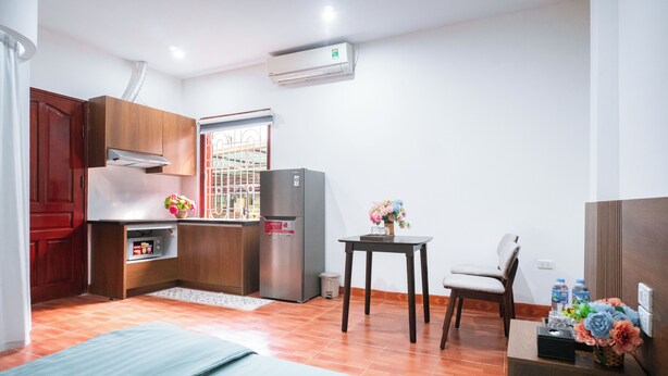 Cocina compacta con refrigerador, ventana con barrotes, una mesa pequeña con una silla y una cama al frente.