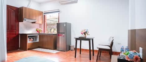 Cocina compacta con refrigerador, ventana con barrotes, una mesa pequeña con una silla y una cama al frente.